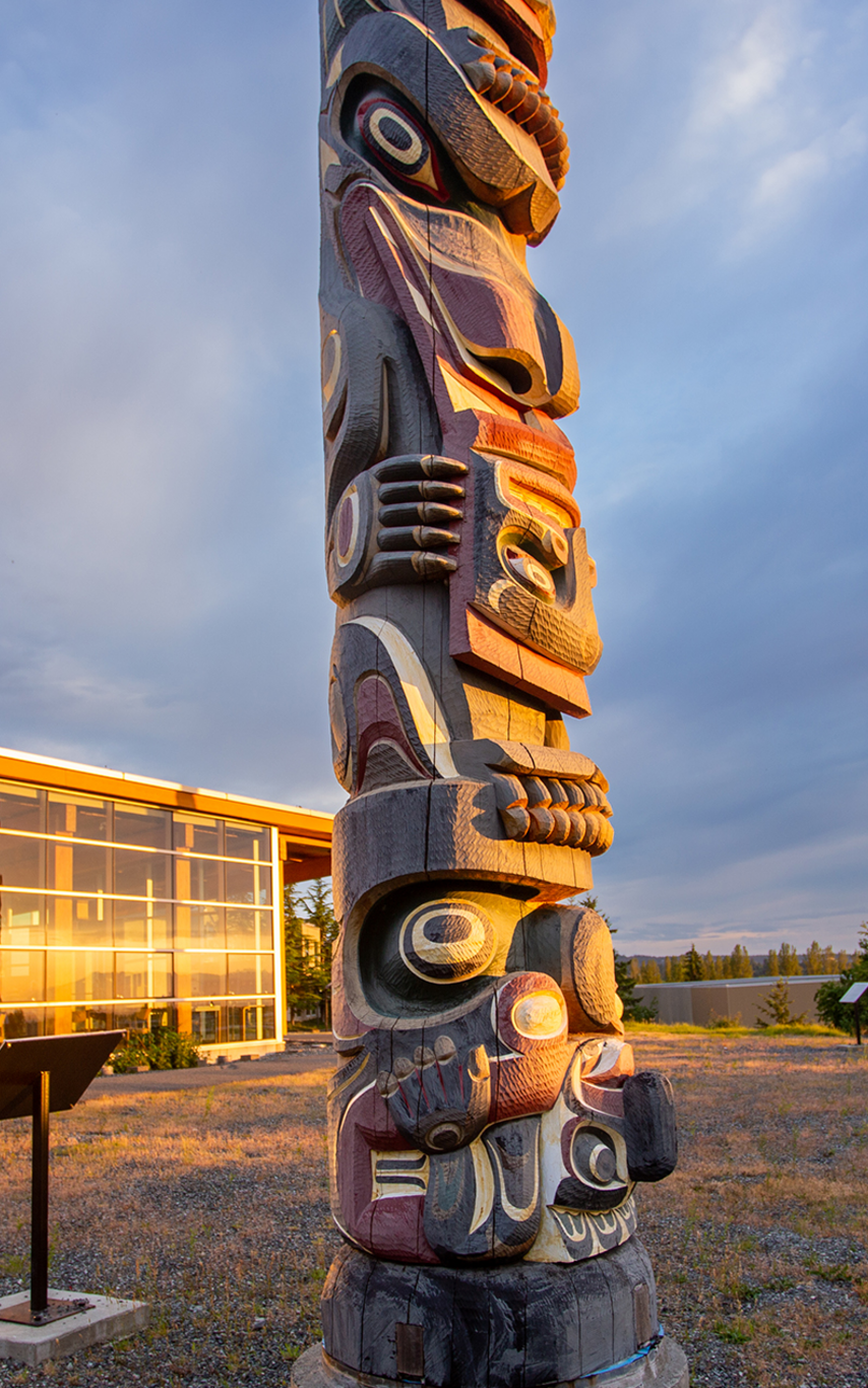 A story pole in front of a glass-walled building reflecting the sun.